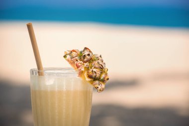 Bardakta alkollü kokteyl ve sahilde ananas dilimi.