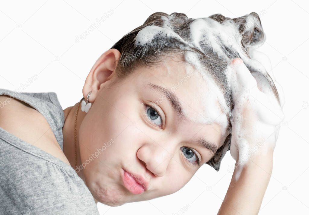Cute little girl lathers hair on her head with shampoo. White background. Cleanliness and hygiene concept