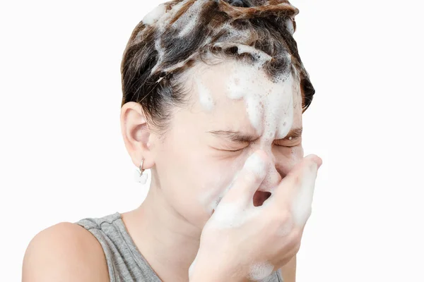 头发上有洗发水 眼睛闭着的女孩在浴室里用手擦拭她的脸 白人背景 — 图库照片