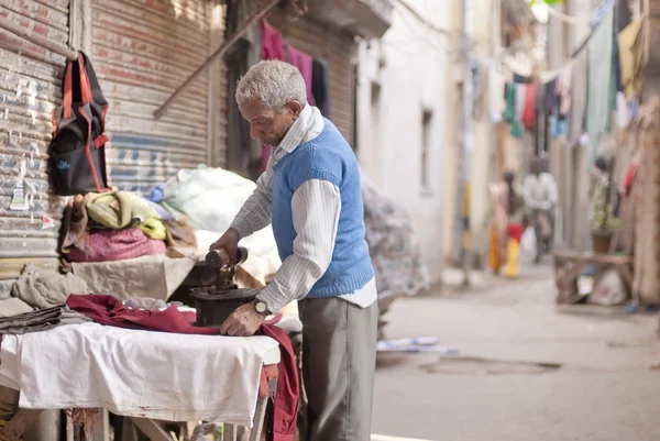 Indian człowiek żelazka ubrania za pomocą żelaza węgiel na ulicy, New Delhi, Indie. — Zdjęcie stockowe