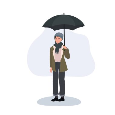 Yağmurlu bir günde elinde sıcak kalmak için kışlık giysiler giymiş bir şemsiye tutan genç bir yetişkin dışarıda duruyor.