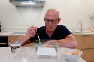 Bir adam mutfakta tek başına salata yiyor..