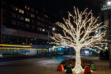 Stockholm, İsveç 'te Sundbybergs' in torg veya meydanında yanan bir Noel ağacı ve gelip geçen bir tramvay.