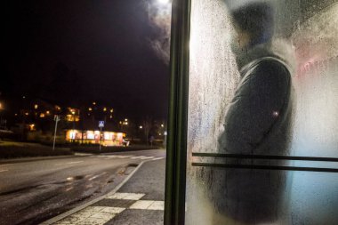 Stockholm, Sweden A man waits for a bus in thr Lidingo suburb in the rain. clipart