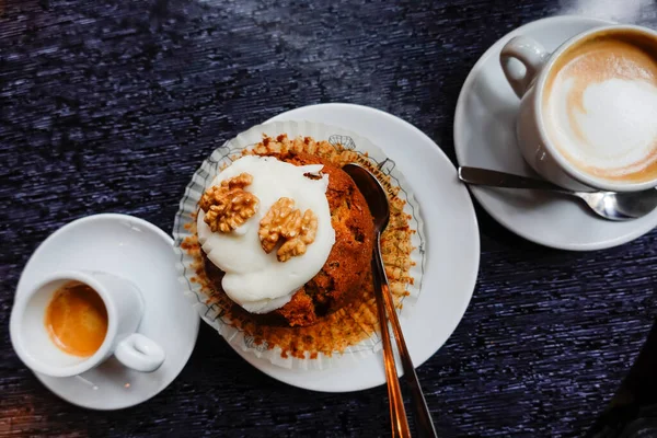 A piece of carrot cake and a cup of espresso coffee and a latte.
