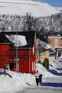 Kiruna, İsveç Karlı bir sokakta koşan bir koşucu ve yerleşim yerlerinde renkli evler.