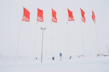 Riksgransen, İsveç Bayrakları ICA süpermarketinin otoparkında kar fırtınası estiriyor ve insanlar yürüyor.