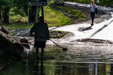 Stockholm, İsveç 'te bir adam, iyi bir yardımsever, şiddetli bir yağış sonrası sel basmış bir yeraltı geçidinde bir süpürgeyle tıkanıklığı açmaya çalışıyor..