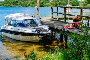 Bir kadın rıhtımda bir köpekle oturuyor, motorsikletin yanında..
