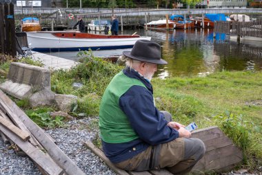 Stockholm, İsveç 11 Ekim 2025 Klasik bir ahşap tekne kış deposu için raylara çıkarıldı. Ve bir voliunteer telefonla oturuyor..