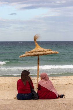 Susa, Tunus 3 Kasım 2025 Rüzgarlı bir günde iki kadın saman şemsiyesinin altında oturuyor.