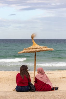 Susa, Tunus 3 Kasım 2025 Rüzgarlı bir günde iki kadın saman şemsiyesinin altında oturuyor.