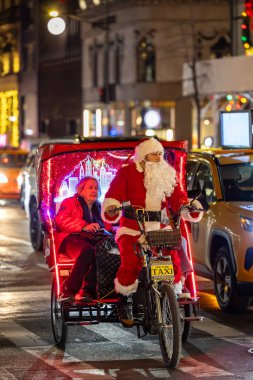 New York, New York, ABD Aralık 2025 Noel Baba gibi giyinmiş bir adam turistler için 5. Cadde 'de bisiklet rickshaw' u kullanıyor..
