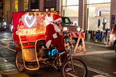 New York, New York, ABD Aralık 2025 Noel Baba gibi giyinmiş bir adam turistler için 5. Cadde 'de bisiklet rickshaw' u kullanıyor..