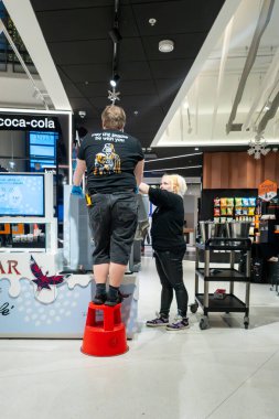 Tallinn, Estonya 15 Aralık 2025 Bir adam taburede duruyor ve bir kadın süpermarkette içki makinesini tamir ediyor.