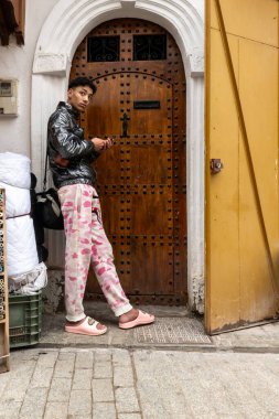 Rabat, Fas 29 Ocak 2026 genç ve modaya uygun bir Faslı cep telefonuyla kapıda duruyor.,