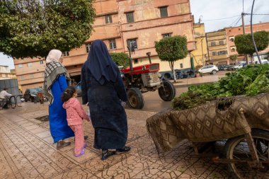 Berrechid, Fas 3 Şubat 2026 İki Arap kadın, park etmiş traktörü ve taze yeşillik arabasıyla sokakta yürüyorlar..