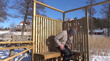 Trosa, İsveç Kış güneşinde bir adam donmuş bir gölün kıyısında, ahşap bir güneş güvertesinde oturur.