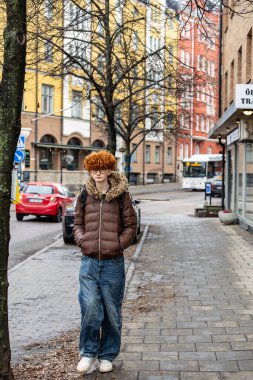 Norrkoping, İsveç. 26 Şubat 2026. Kızıl saçlı genç bir adam şehir merkezinde yürüyor..