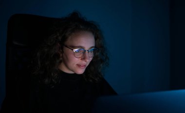 Geceleri bilgisayarla çalışan bir kadın. Karanlık ve mavi ışık var. Fazla çalışma kavramı.