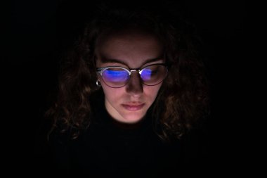 Bilgisayar ekranı, gece çalışan bir kadının gözlüklerini yansıtıyor. Fazla çalışma kavramı.