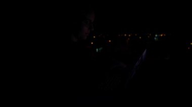 4K, kulaklıklı bir kadın bilgisayarını açar ve bir gecede yazmaya başlar. O yüksek bir binada, ekranın ışığı yüzüne yansıyor..