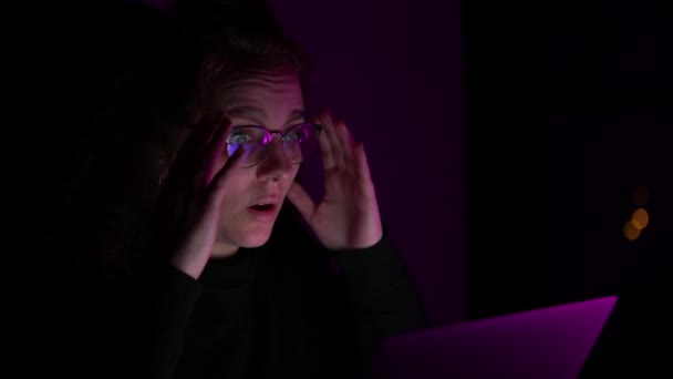 圧倒された女性は自分のコンピュータ上で閲覧している間に彼女の頭に手を上げます 夜になると暗くなる 異なる色のライトがあります — ストック動画