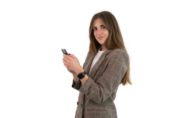 Takım elbiseli bir iş kadını beyaz arka planda izole bir şekilde akıllı telefonuyla yazı yazıyor. Kadın elleriyle cep telefonunu tutarken kameraya bakıyor.