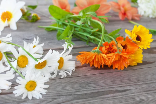 Camomilla, calendula e altri fiori da giardino per un mazzo su un tavolo di legno sullo sfondo di un giardino estivo Foto Stock