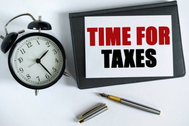 İş ve olumlu kavram. Masanın üzerinde bir saat, bir kalem, bir defter ve yazılı bir kart var - Vergiler için zaman