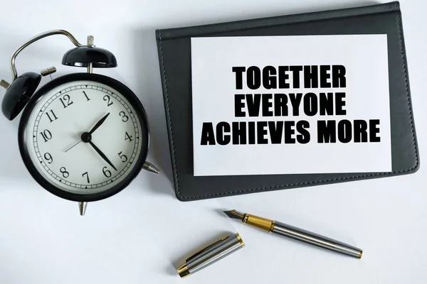 Business and positive concept. On the table there is a clock, a pen, a notebook and a card on which the text is written - TOGETHER EVERYONE ACHIEVES MORE