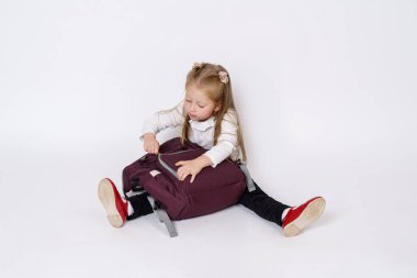 Çocuk konsepti. Kız yere oturur ve çantasını açar. Beyaz arkaplan üzerinde izole edilmiş.