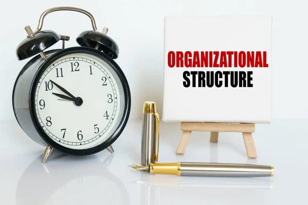 Business and finance concept. On the table there is a clock, a pen and a stand with a card on which the text is written - ORGANIZATIONAL STRUCTURE