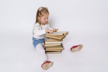 Eğitim ve insan kavramı. Kitapların yanına oturup kitap okuyan genç bir kızın portresi. Beyaz arkaplan üzerinde izole edilmiş.