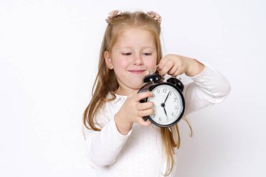 Çocuk konsepti. Bir kız elinde çalar saati tutuyor ve onunla oynuyor. Beyaz arkaplan üzerinde izole edilmiş.