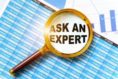 Finans ve iş konsepti. Mali raporlar, çizelgeler ve bir büyüteç masada. Büyütecin içinde bir yazı var - Bir Uzmana Sorun