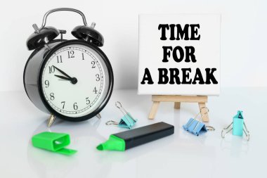 Zaman kavramı. Masanın üzerinde bir çalar saat, bir keçeli kalem ve üzerinde yazılı bir tuval olan bir üçayak var.