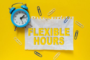 İş ve finans kavramı. Masanın üzerinde bir çalar saat, ataçlar ve üzerinde FLEXIBLE saatleri yazan bir kağıt parçası var. Sarı arkaplan.