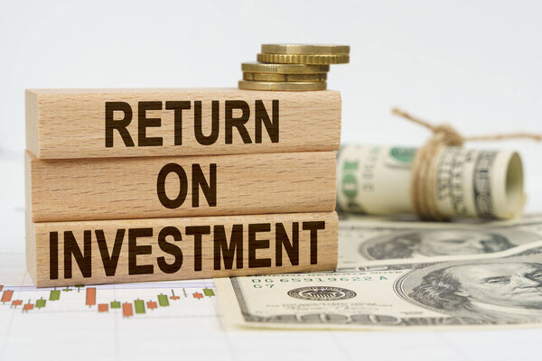Business and finance concept. On the table are dollars, financial charts and wooden plates on which it is written - RETURN ON INVESTMENT