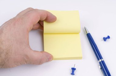 Bir adamın eli not kağıdına göz atar. Masanın üzerinde kağıt, düğmeler ve bir kalem var..