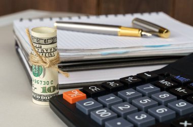 İş ve finans kavramı. Masanın üzerinde, hesap makinesinin yanında dolar ve kalemle birlikte bir defter var.