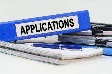 İş ve finans kavramı. Masanın üzerinde bir defter, bir kalem, belgeler ve üzerinde APPLICATIONS yazan bir klasör var.