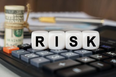 İş ve finans kavramı. Hesap makinesinde RISK yazan küpler var. Yakınlarda odak dışı - dolar, defter ve kalem