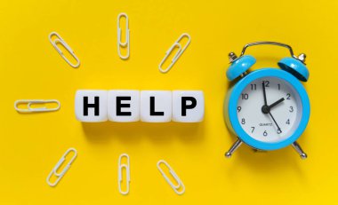 Finans ve ekonomi kavramı. Sarı arkaplanda, mavi alarmlı saat, ataç ve beyaz küplerin üzerine yazı yazılmış - Yardım et