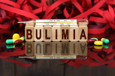 Tıp ve sağlık konsepti. Yüzeyde görülebilir haplar, bir termometre, ahşap ölür ve üzerine yazılan yansımaları - BULIMIA