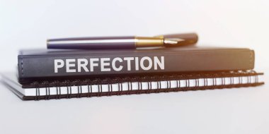 İş ve finans kavramı. Masanın üzerinde bir defter, bir kalem ve bir kitap var. Kitap diyor ki - Mükemmellik