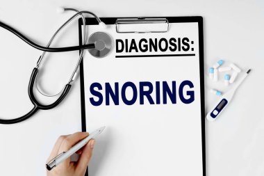 Tıp ve sağlık konsepti. Masanın üzerinde bir stetoskop, bir hap termometresi ve bir teşhis kağıdı var. Metin kağıdın üzerine şu teşhisle yazılmıştır: SNORING