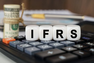 İş ve finans kavramı. Hesap makinesinde IFRS yazan küpler var. Yakınlarda odak dışı - dolar, defter ve kalem