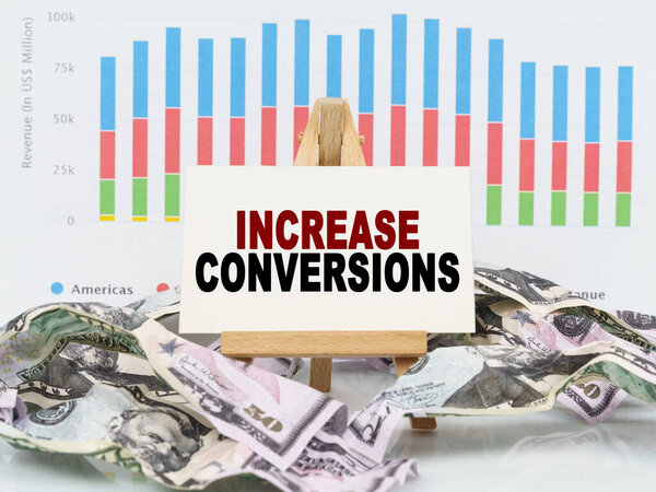 Business and finance concept. Among financial charts and money is a sign with the text - INCREASE CONVERSIONS