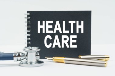 Tıp ve sağlık konsepti. Beyaz arkaplanda stetoskop, kalem ve siyah bir defter bulunur.